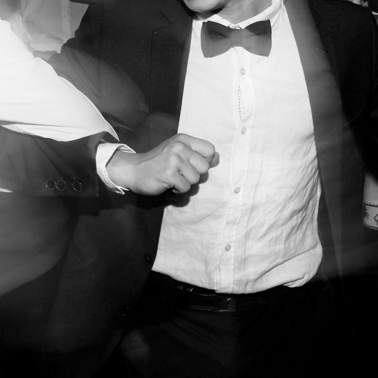 Abiball Mann in Anzug mit Fliege, gefasst in Bewegung mit erhobener Hand