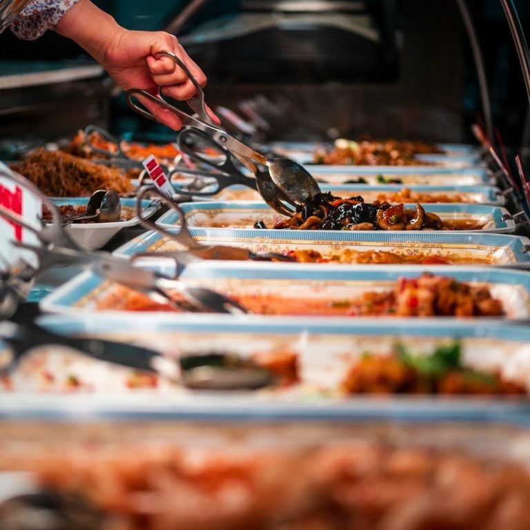 Buffet Buffet mit verschiedenen Gerichten, eine Hand nimmt Essen mit Zangen.